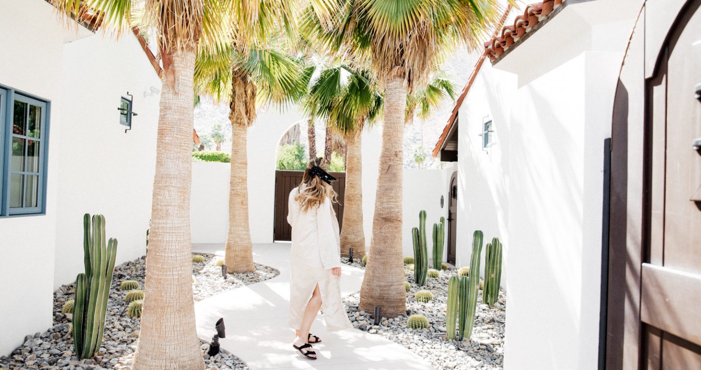 Erin walking in a bright courtyard with cacti and palm trees