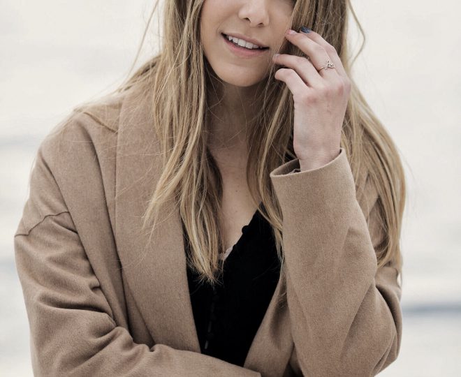 Erin smiling at the camera while wearing an oversized cardigan and statement jewelry.