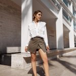 Erin posing while wearing a white blouse, tan skirt and red high heels with hair styled in a bun.