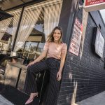 Erin posing outside a cafe with striped pants, a blush shirt, and pink heels on.