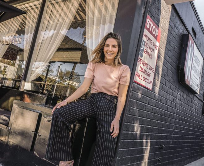 Erin posing outside a cafe with striped pants, a blush shirt, and pink heels on.