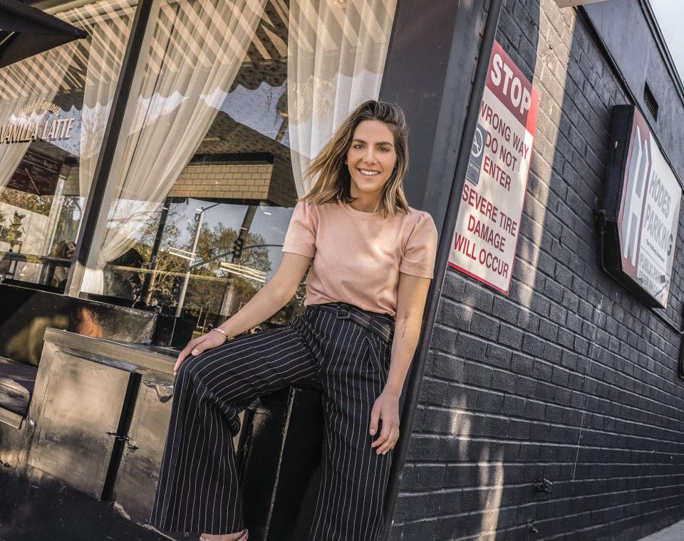 Erin posing outside a cafe with striped pants, a blush shirt, and pink heels on.