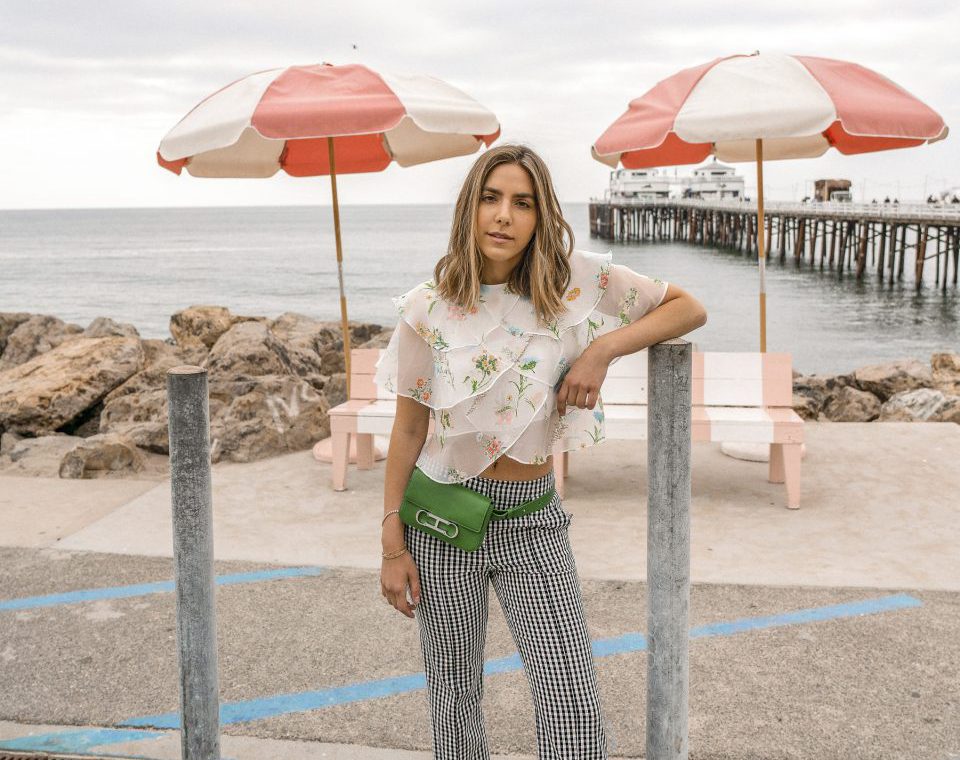 Erin in a floral blouse and checkered pants and a green fanny pack