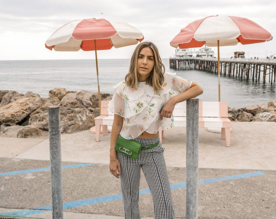 Erin in a floral blouse and checkered pants and a green fanny pack