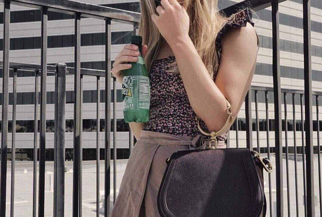 Erin standing outside in a dress holding a bottle of Perrier