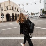 Erin crossing the street and wearing a patterned black suit with white sneakers and a black leather backpack