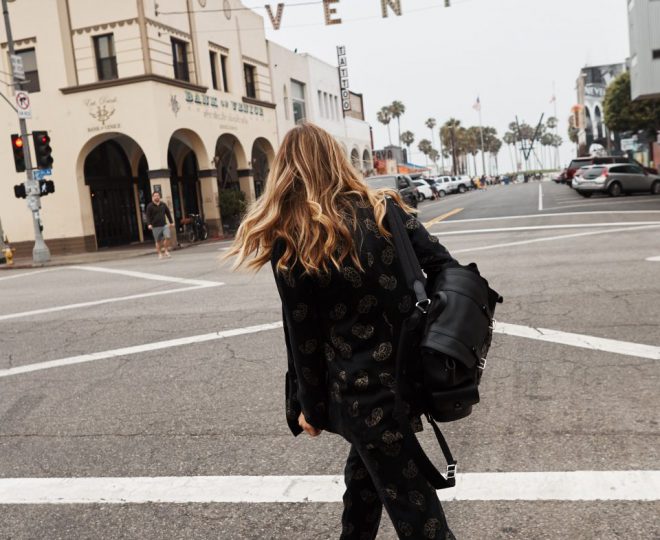 Erin crossing the street and wearing a patterned black suit with white sneakers and a black leather backpack