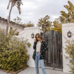 Erin in a patterned blazer and light blue jeans looking over the top of her sunglasses.