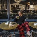 Erin sitting at a cafe table drinking tea and wearing a black long sleeve shirt and red plaid pants with pink high heels.