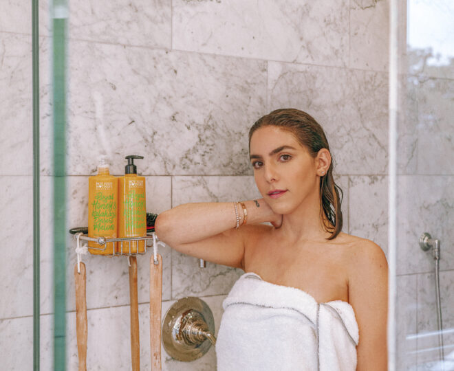 Erin standing in the shower with a white towel wrapped around her. Not Your Mother's shampoo is in the background.