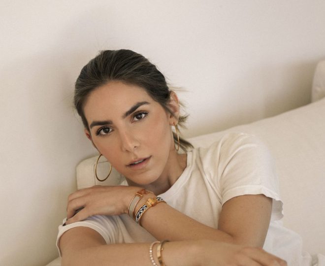 Erin wearing a white shirt witting on a white couch. Her hair is pulled back and she is wearing minimal makeup with eyeshadow and blush.