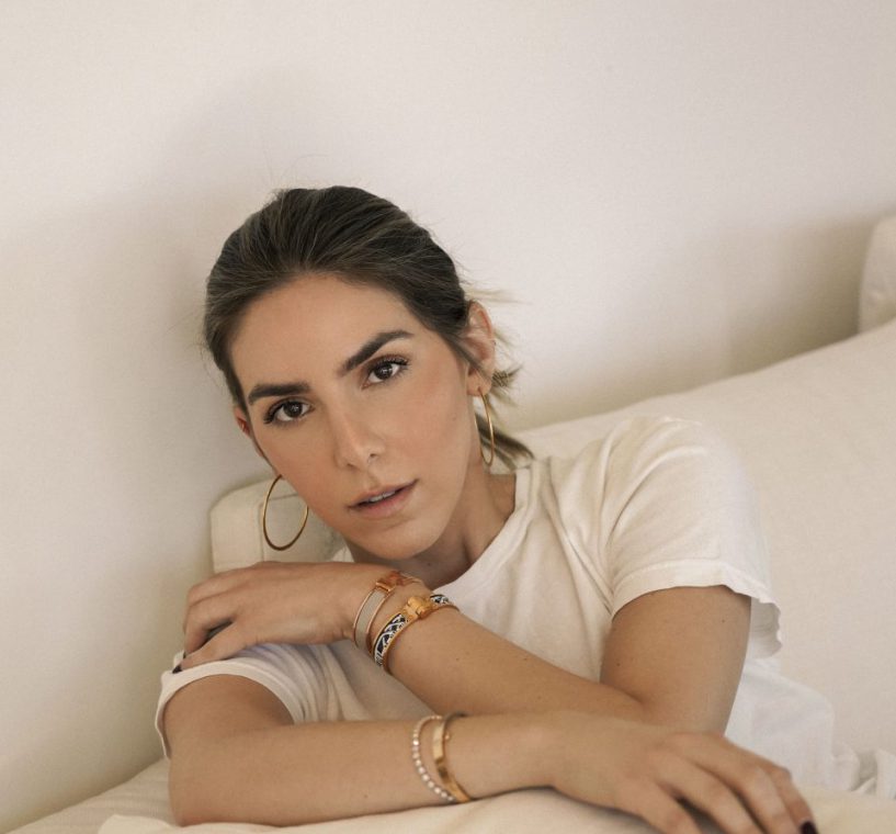 Erin wearing a white shirt witting on a white couch. Her hair is pulled back and she is wearing minimal makeup with eyeshadow and blush.