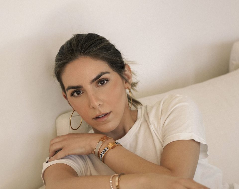 Erin wearing a white shirt witting on a white couch. Her hair is pulled back and she is wearing minimal makeup with eyeshadow and blush.