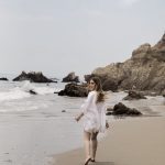 Erin walking along the beach in a white cover up, looking back over her shoulder.