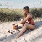 Erin sitting on the beach in a red polka dot bikini.