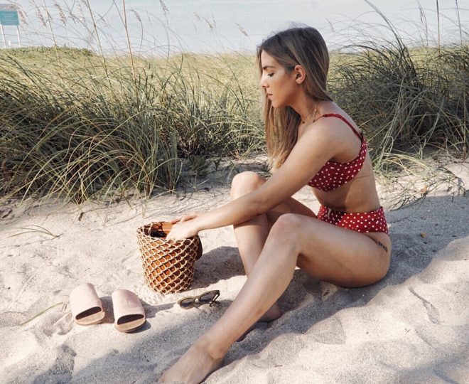 Erin sitting on the beach in a red polka dot bikini.